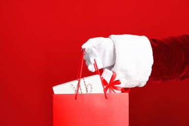 Santa holding paper bag with gift boxes on red background, closeup