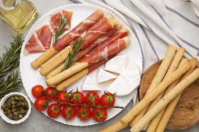 Photo of Delicious grissini sticks with prosciutto and snacks on grey table, flat lay