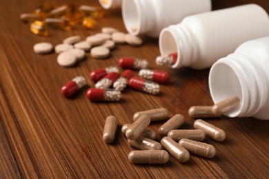 Overturned bottles with different dietary supplements on wooden table, closeup
