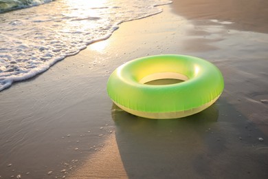 Light green inflatable ring on sunlit sandy beach near sea, space for text
