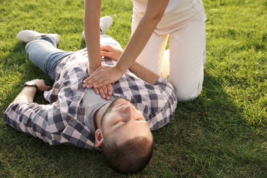 Woman doing cardiac massage to unconscious man with heart attack on green lawn