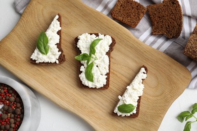 Photo of Bread with cottage cheese and basil on white table, flat lay