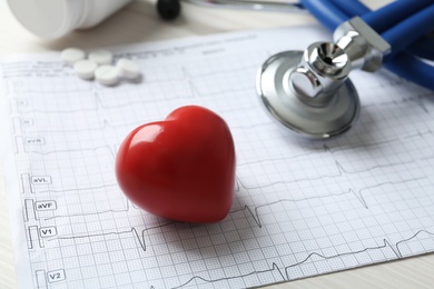 Cardiogram report, red decorative heart and stethoscope on table, closeup