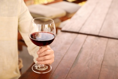 Woman with glass of red wine in outdoor cafe, closeup. Space for text