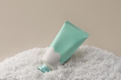 Photo of Winter skin care. Hand cream on artificial snow against light grey background