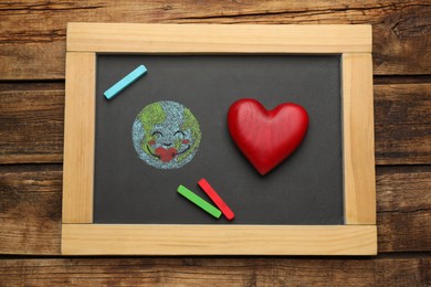 Happy Earth Day. Blackboard with drawing of planet, decorative heart and chalk pieces on wooden table, top view