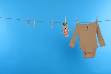 Photo of Baby onesie and bear toy drying on laundry line against light blue background, space for text