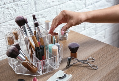 Woman taking cosmetics from organizer for makeup products on table