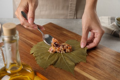 Woman preparing stuffed grape leaves on wooden board, closeup