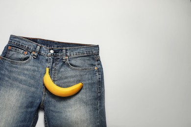Men jeans with banana on light grey background, top view and space for text. Potency concept