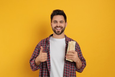 Photo of Happy young man with tasty shawarma showing thumb up on yellow background