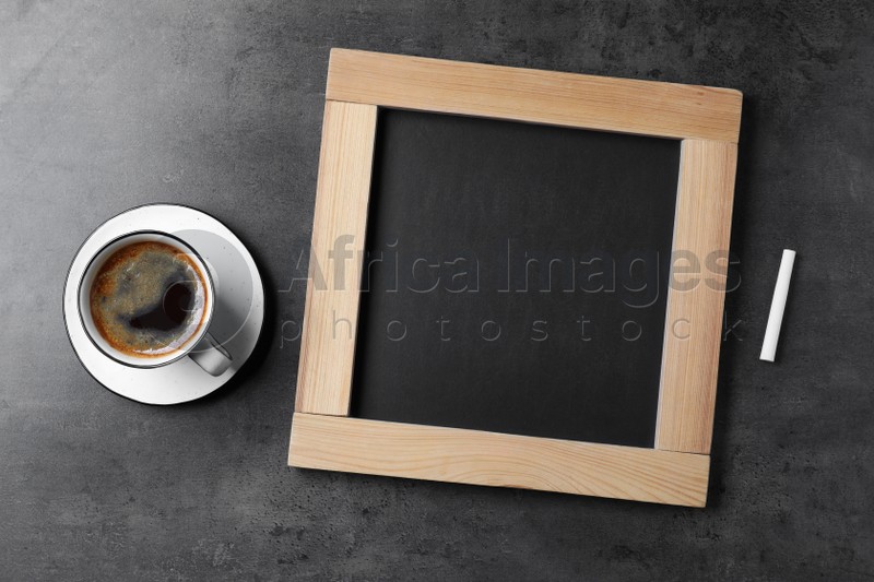 Clean small blackboard, chalk and cup of coffee on grey table, flat lay