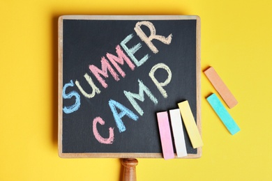 Words SUMMER CAMP written with colorful chalk on small blackboard, top view