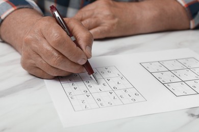 Senior man solving sudoku puzzle at white marble table, closeup