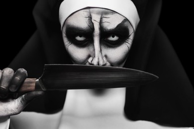 Scary devilish nun with knife on black background, closeup. Halloween party look