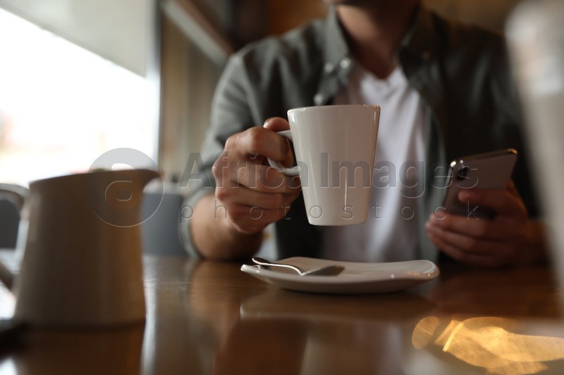 Man with cup of coffee and smartphone at table in morning, closeup