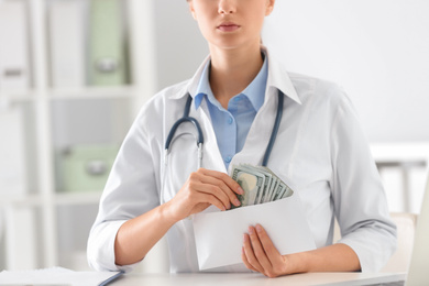 Doctor with bribe at desk in clinic, closeup. Corrupted medicine