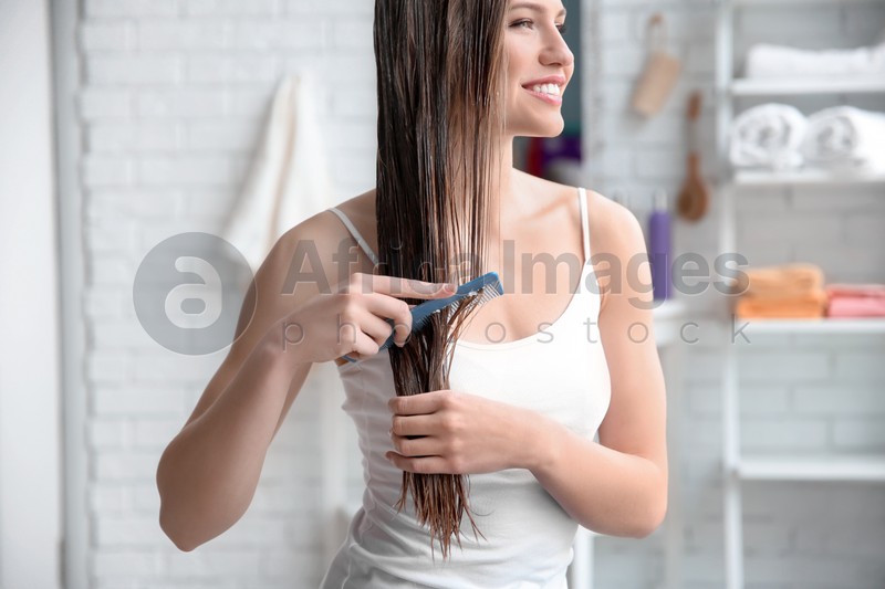 Young woman brushing hair after applying mask in bathroom