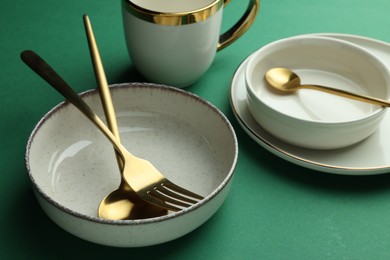 Photo of Stylish empty dishware and golden cutlery on green background