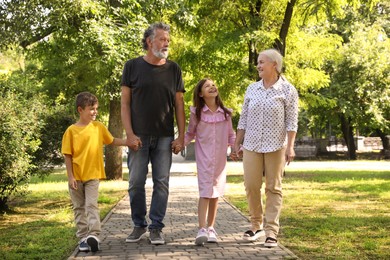 Photo of Happy grandparents with little children walking together in park