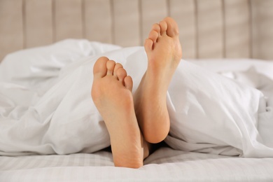 Person in bed with white linens at home, closeup on feet