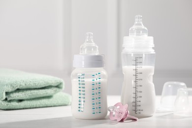 Photo of Feeding bottles with milk, pacifier and towel on white wooden table