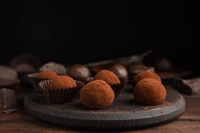 Delicious chocolate truffles powdered with cocoa on wooden table, space for text