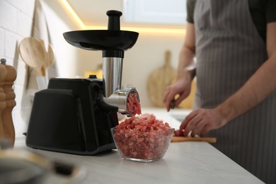 Closeup view of man cutting ingredients in kitchen, focus on meat grinder