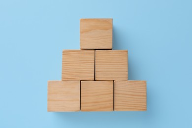 Photo of Pyramid made of wooden cubes on light blue background, top view. Management concept