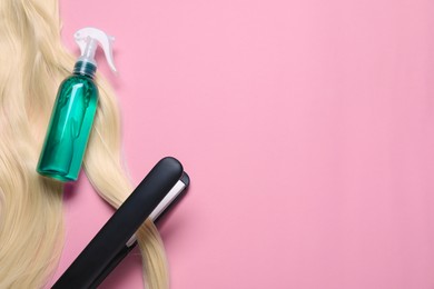 Photo of Spray bottle with thermal protection, iron and lock of blonde hair on pink background, flat lay. Space for text