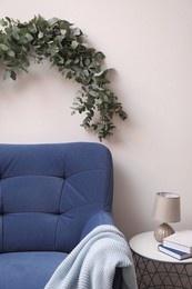 Beautiful garland made of eucalyptus branches hanging above armchair on white wall indoors
