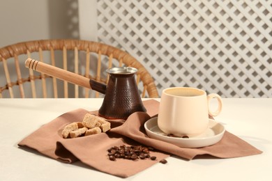 Photo of Turkish coffee. Cezve and cup with hot aromatic coffee, beans and sugar on white wooden table