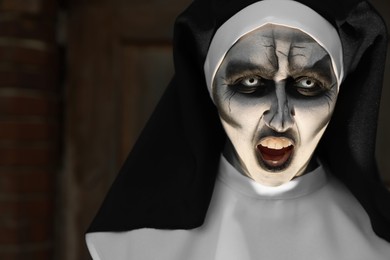 Photo of Portrait of scary devilish nun on blurred background, space for text. Halloween party look