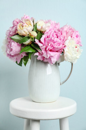 Beautiful peonies in jug on white stool against light blue background