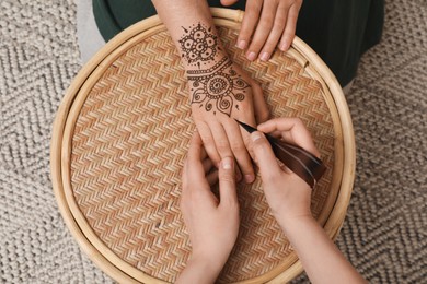 Master making henna tattoo on hand at table, top view. Traditional mehndi
