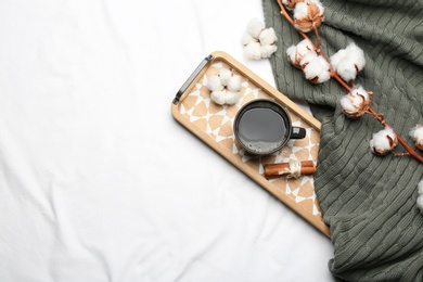 Flat lay composition with hot drink and warm plaid on white bedsheet, space for text
