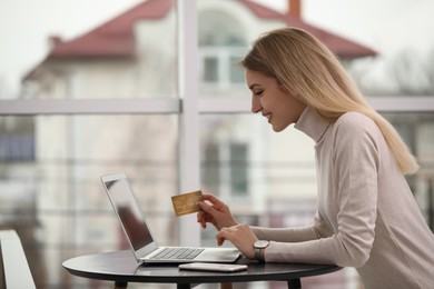 Woman with credit card using laptop for online shopping indoors