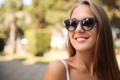 Beautiful young woman in stylish sunglasses outdoors, space for text
