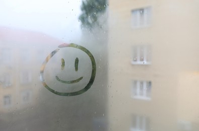 Funny face drawn on foggy window, space for text. Rainy weather