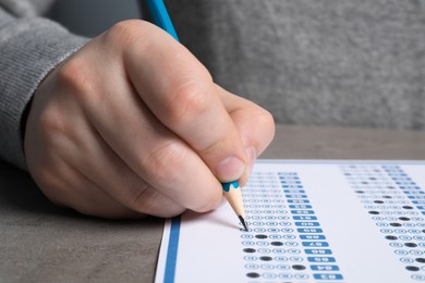 Photo of Student filling answer sheet at grey table, closeup. Passing exam