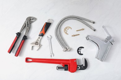Parts of water tap and wrenches on white marble countertop, flat lay