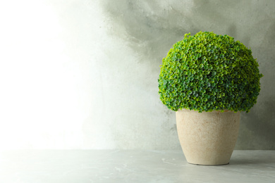 Artificial plant in ceramic flower pot on light marble table. Space for text