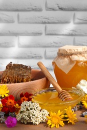 Delicious honey, combs and different flowers on wooden table near white brick wall