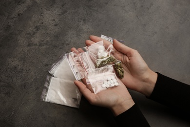Woman holding plastic bags with cocaine, pills and hemp buds on grey background, closeup