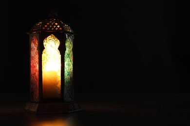 Decorative Arabic lantern on table against black background, space for text