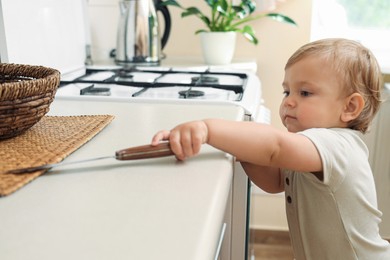 Photo of Little child holding sharp knife in kitchen. Dangerous situation
