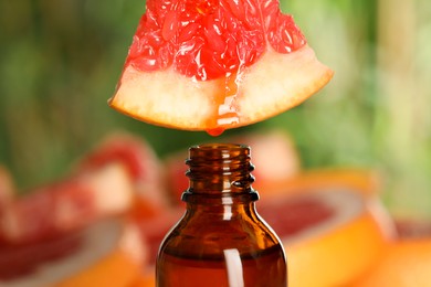 Dripping essential oil from grapefruit into bottle on blurred background, closeup