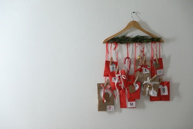 Handmade Advent calendar with gifts hanging on white wall, space for text. Christmas season