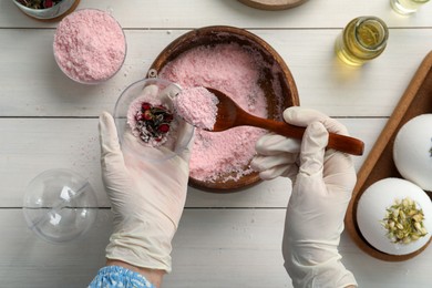 Woman in gloves making bath bomb at white wooden table, top view