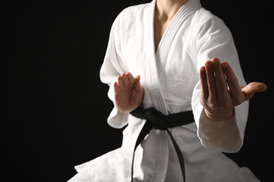 Man wearing keikogi and black belt on dark background, closeup. Martial arts uniform
